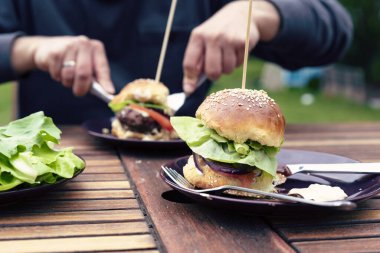 Bahçede sosis yiyen bir adam. Sağlıklı öğle yemeğinde ev yapımı börek. Elleri masa üstünde barbekü için hazır yemek. Kapat..