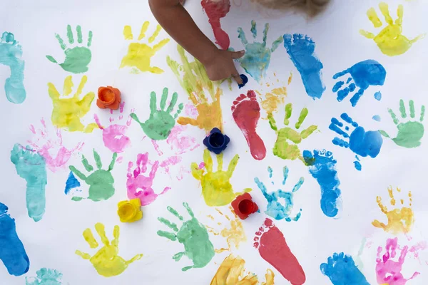 Sensory play of children. Little child imprint colorful palm and foot on white background. Hand of girl paints artictic artwork. Childhood and colors of fun.