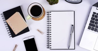 Boş defterli iş ve teknoloji ve model telefonlu telefon. Bir fincan kahve ve beyaz bir kitap kağıdıyla ofis masası. Düz nad üst görünüm yatıyordu.
