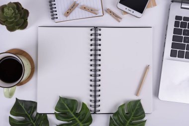 Kahve fincanlı ofis masası, boş ekranlı akıllı telefon ve dizüstü bilgisayar. Tahta kalemli ve yazı yazmak için yeri olan sarmal defter. Üst görünüm.