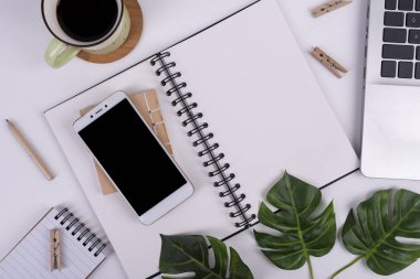 Kahve fincanlı ofis masası, boş ekranlı akıllı telefon ve dizüstü bilgisayar. Tahta kalemli ve yazı yazmak için yeri olan sarmal defter. Üst görünüm.