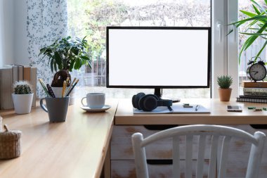 Beyaz duvarlı, şık iş odasındaki ahşap ofis masasındaki bilgisayardaki boş monitör ekranı. Eski tarz bitkiler ve dizüstü bilgisayarlarla ofis alanının hafif bir iç mekanı. 