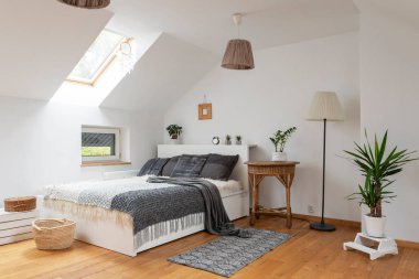 Çift kişilik yataklı ve gri yastıklı modern yatak odası. Tavan arasında İskandinav tarzı beyaz yatak odası.