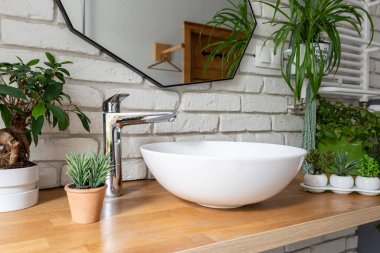 Banyo içi endüstriyel tarzda beyaz tuğla duvar, ayna, yeşil bitkiler, lavabo ve ahşap tezgah. Modern banyo.