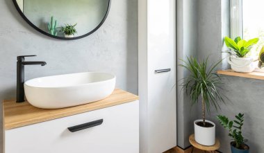 Modern banyo içinde pencereli lavabosu olan seramik bir lavabo. Gri duvardaki yuvarlak ayna. Banyoda yeşil bitkiler.