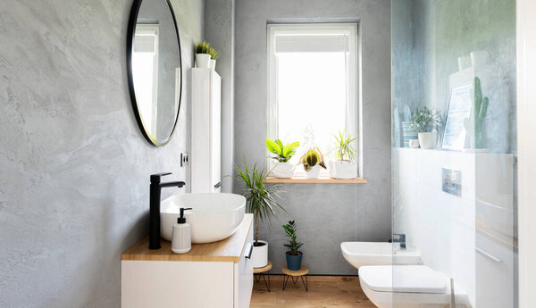 Modern bathroom with stylish design. Washroom in cozy interior with ceramic washbasin, toilet and bidet. Room spa with window and green plants.