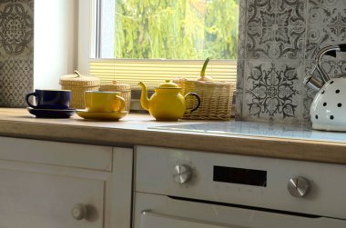 Mutfakta, ahşap tezgahta bir fincan çay. Pencereli, fırınlı ve desenli fayanslı mutfak..