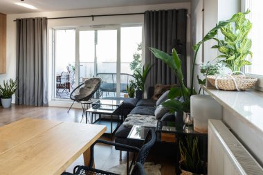 Modern oturma odası, büyük pencereli şık bir iç mekan. Ahşap zeminde rahat bir kanepe ve konforlu bir dairede yeşil bir bitki..