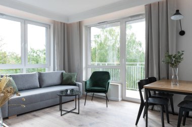 Oturma odasının içinde, şık bir dairede yemek masası var. Ahşap zemin ve pencereli rahat bir kanepe. Modern biçim.