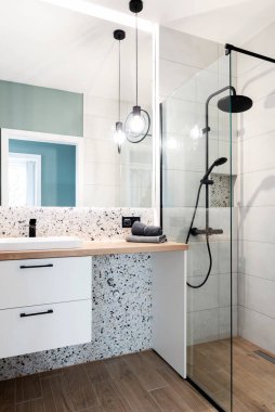 Bathroom with ceramic bathroom sink on wooden counter on cupboard, mirror on the wall and modern shower with glass. Interior of washroom. Hotel.Vertical clipart