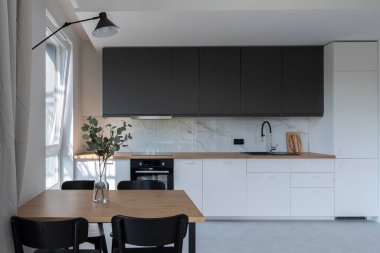 Duvarında mermer ve sandalyeli yemek masası olan lüks bir mutfak. Pencereli yeni dairede beyaz mobilyalar ve ahşap tezgah.