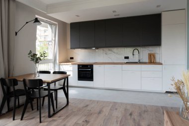 Duvarında mermer ve sandalyeli yemek masası olan lüks bir mutfak. Pencereli yeni dairede beyaz mobilyalar ve ahşap tezgah.