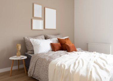 Comfortable double bed with orange piloows, white bedding and blanket in cozy bedroom. Stylish interior in hotel with frame on the wall. Modern room in apartment at home.