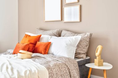 Comfortable double bed with red piloows, white bedding and blanket in cozy bedroom. Stylish interior in hotel with frame on the wall. Modern room in apartment at home.