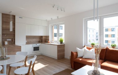 Kitchen interior with white furniture in scandinavian design and dining room with table and chairs. Interior with wooden floor and window in new apartment in luxurious style.