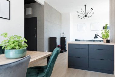 Stylish interior of room with dining room and living room. White wall with frame and table with chairs in stylish apartment.