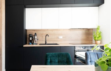 Modern interior of kitchen with stylish black and white furniture with kitchen sink in the wooden counter and green plant on the table. Luxurious design of chairs.