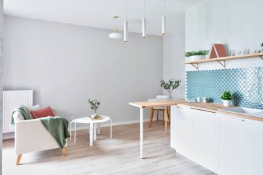 Modern kitchen with living room in design interior. Stylish kitchen with white cabinets, wooden counter and floor and texture tiles on the wall.