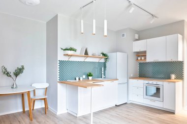 Modern interior of new kitchen with white furniture and cabinets and wooden kitchen counter. Stylish lamp and wooden floor in contemporary indoor. Oven, texture tiles on the wall and decoration.