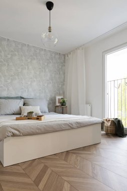 Rahat yataklı, yastıklı, pencereli ve duvarında tasarım duvar kağıtları olan rahat bir yatak odası. İçi parke ile ahşap zemin. Hiç kimse ve dikey.