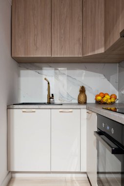 Mutfak içinde ahşap mobilyalar ve duvarda mermer var. Fırını ve dolapları olan şık küçük bir mutfak..