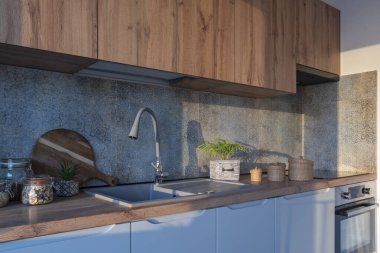 Modern mobilyaları olan, ahşap dolapları ve tezgahı olan ve duvarında desenli fayanslar olan şık bir mutfak. Güneş ışığıyla yeni bir daire.