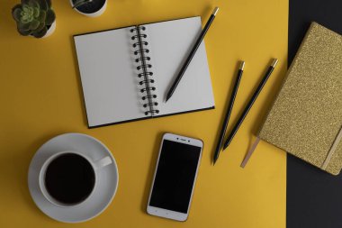 Siyah ekranlı, klavyeli, not defterli ve kahveli modern siyah ve sarı ofis masası. Kopyalama alanı olan üst görünüm, düz yatay.