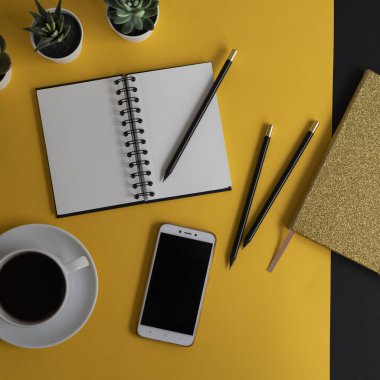 Siyah ekranlı, klavyeli, not defterli ve kahveli modern siyah ve sarı ofis masası. Kopyalama alanı olan üst görünüm, düz yatay.