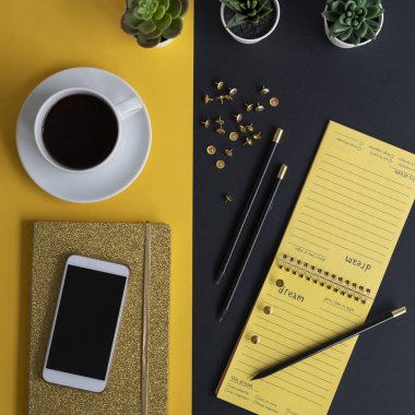 Siyah ekranlı, klavyeli, not defterli ve kahveli modern siyah ve sarı ofis masası. Kopyalama alanı olan üst görünüm, düz yatay.