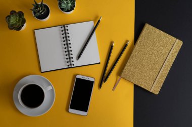 Siyah ekranlı, klavyeli, not defterli ve kahveli modern siyah ve sarı ofis masası. Kopyalama alanı olan üst görünüm, düz yatay.