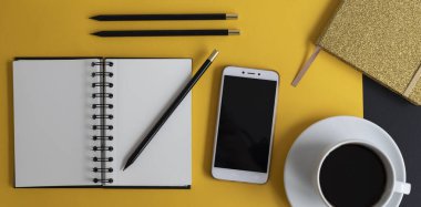 Siyah ekranlı, klavyeli, not defterli ve kahveli modern siyah ve sarı ofis masası. Kopyalama alanı olan üst görünüm, düz yatay.