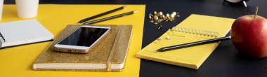 Modern ofis bilgisayarında akıllı telefon, defter ve elma var. Masanın sarı ve siyah tasarımı. Panoramik pankart.