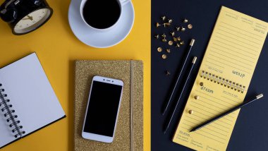 Siyah ekranlı, klavyeli, not defterli ve kahveli modern siyah ve sarı ofis masası. Kopyalama alanı olan üst görünüm, düz yatay.