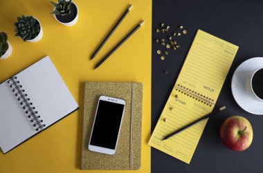 Siyah ekranlı, klavyeli, not defterli ve kahveli modern siyah ve sarı ofis masası. Kopyalama alanı olan üst görünüm, düz yatay.