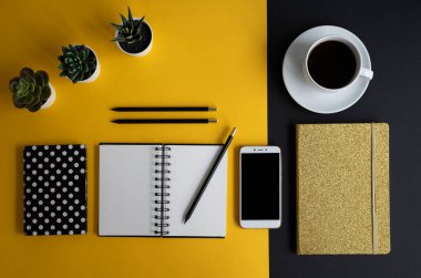 Siyah ekranlı, klavyeli, not defterli ve kahveli modern siyah ve sarı ofis masası. Kopyalama alanı olan üst görünüm, düz yatay.