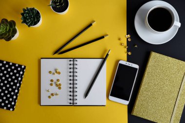 Siyah ekranlı, klavyeli, not defterli ve kahveli modern siyah ve sarı ofis masası. Kopyalama alanı olan üst görünüm, düz yatay.