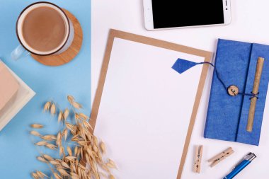 Beyaz ve mavi arkaplanda boş defter, kalem, kahve ve telefon bulunan yaratıcı ofis masası. Panoramik pankart ve üst görünüm.