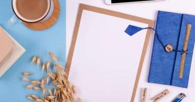 Beyaz ve mavi arkaplanda boş defter, kalem, kahve ve telefon bulunan yaratıcı ofis masası. Panoramik pankart ve üst görünüm.