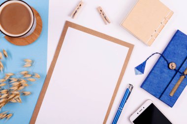 Beyaz ve mavi arkaplanda boş defter, kalem, kahve ve telefon bulunan yaratıcı ofis masası. Panoramik pankart ve üst görünüm.