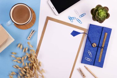 Beyaz ve mavi arkaplanda boş defter, kalem, kahve ve telefon bulunan yaratıcı ofis masası. Panoramik pankart ve üst görünüm.