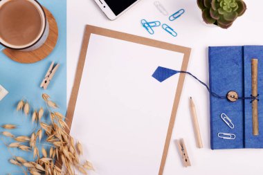 Beyaz ve mavi arkaplanda boş defter, kalem, kahve ve telefon bulunan yaratıcı ofis masası. Panoramik pankart ve üst görünüm.