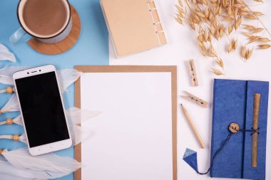 Beyaz ve mavi arkaplanda boş defter, kalem, kahve ve telefon bulunan yaratıcı ofis masası. Panoramik pankart ve üst görünüm.