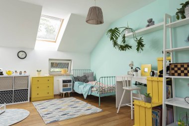 Odanın içi rahat, duvarında pastel rengi ve dekorunda sarı renk olan bir çocuk. Çatı katında yatak, masa ve halı modern tasarımda. İskandinav konsepti.