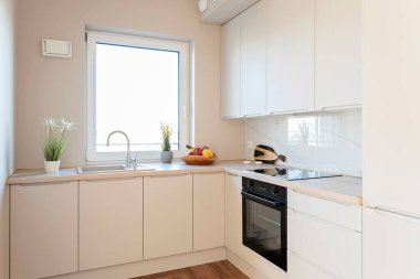 Modern mutfak içi mutfak lavabosu pencerenin yanında musluk, bej dolaplar ve fırın ve ahşap mobilyalarla dolu. Yeni daire ve emlak.