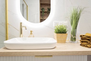 Seramik banyo lavabosu, tezgahında altın musluğu ve modern aynası olan lüks bir banyo. Yeni apartman ve otelde çağdaş iç mekan..