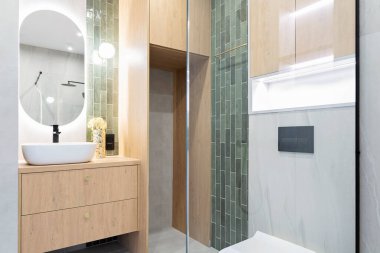 Yeşil fayanslı modern banyo, cam, ayna ve dolapta seramik yıkama leğeni. Şık bir evin tasarımı.