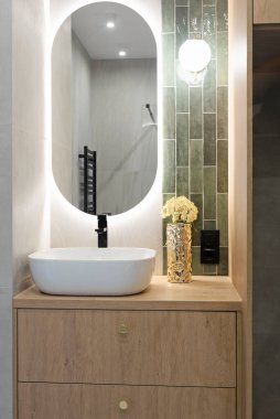 Ahşap dolapta seramik lavabo ve beyaz duvarda ayna. Dairede modern tasarım. Lüks. Dikey.