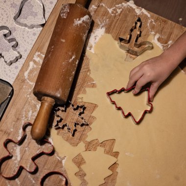 Noel kurabiyesi hamuru ve Noel kurabiyeleri için farklı şekillerde hazırlamak ve kesmek. Evdeki masada merdane ve un taşıyan küçük fırıncı..