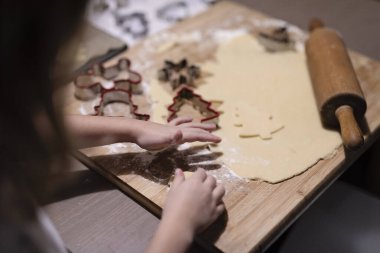 Girl with prepare dough for christmas cookie. Little child creates christmas shape for homemade cookies on table with christmas tree at home. clipart