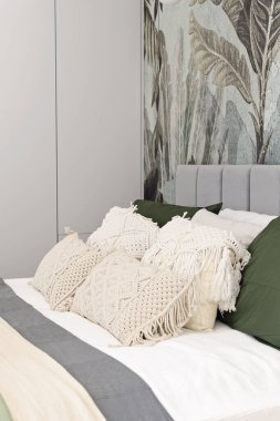 Güzel ve minimalist iç mekanlarda boho yastıklı çift kişilik yatak odasının içi. Duvarında desenli duvar kağıdı olan modern bir ev ve otel odası. Şık mimari. Dikey.